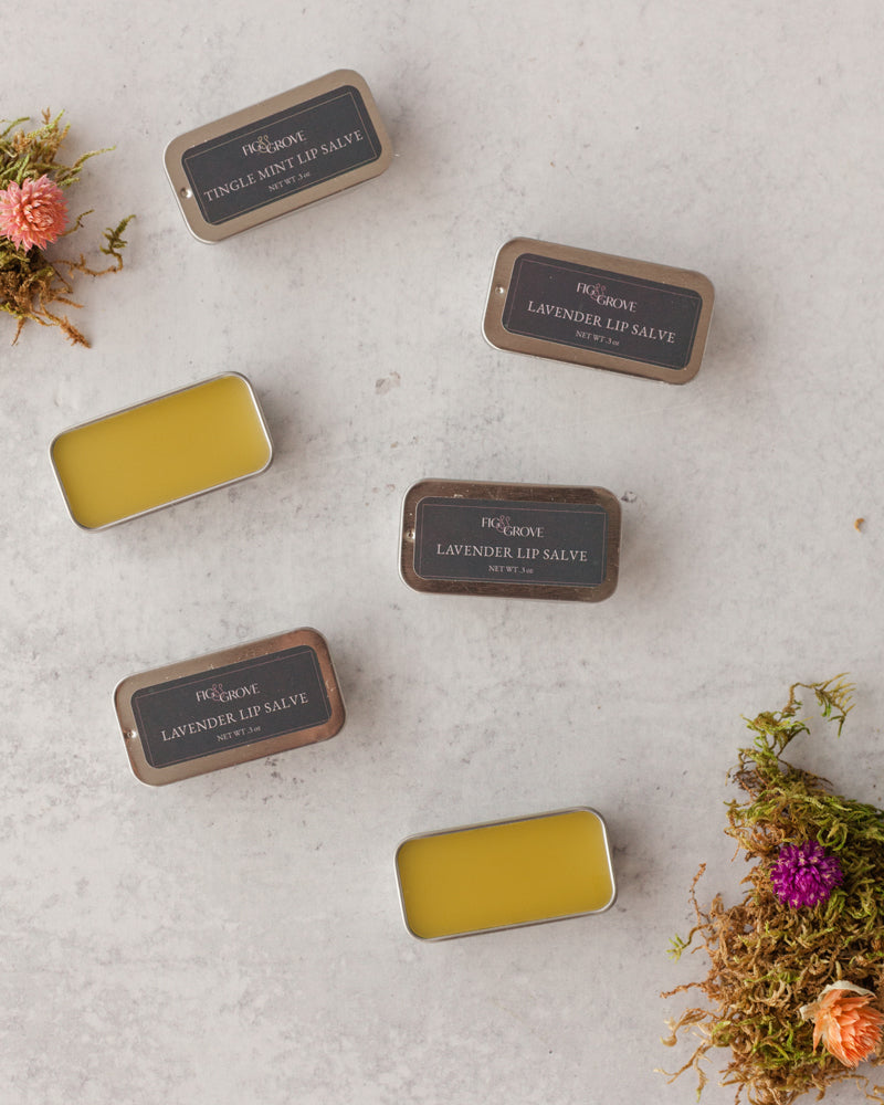 Collection of lip balm tins on a textured surface with floral elements - Fig & Grove