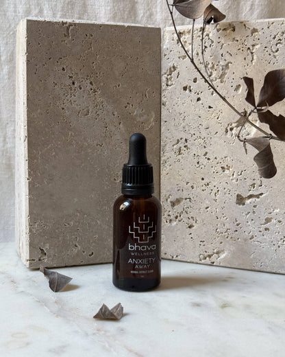 Bhava Anxiety Away dropper bottle on a marble surface with a concrete block and dried leaves in the background.