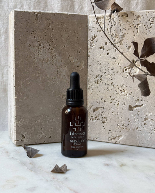 Bhava Anxiety Away dropper bottle on a marble surface with a concrete block and dried leaves in the background.