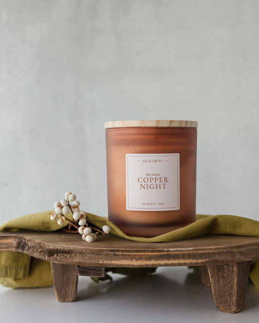 Copper Night candle in amber glass jar on wood table evoking roasted chestnuts and warm spiced rum – Fig & Grove