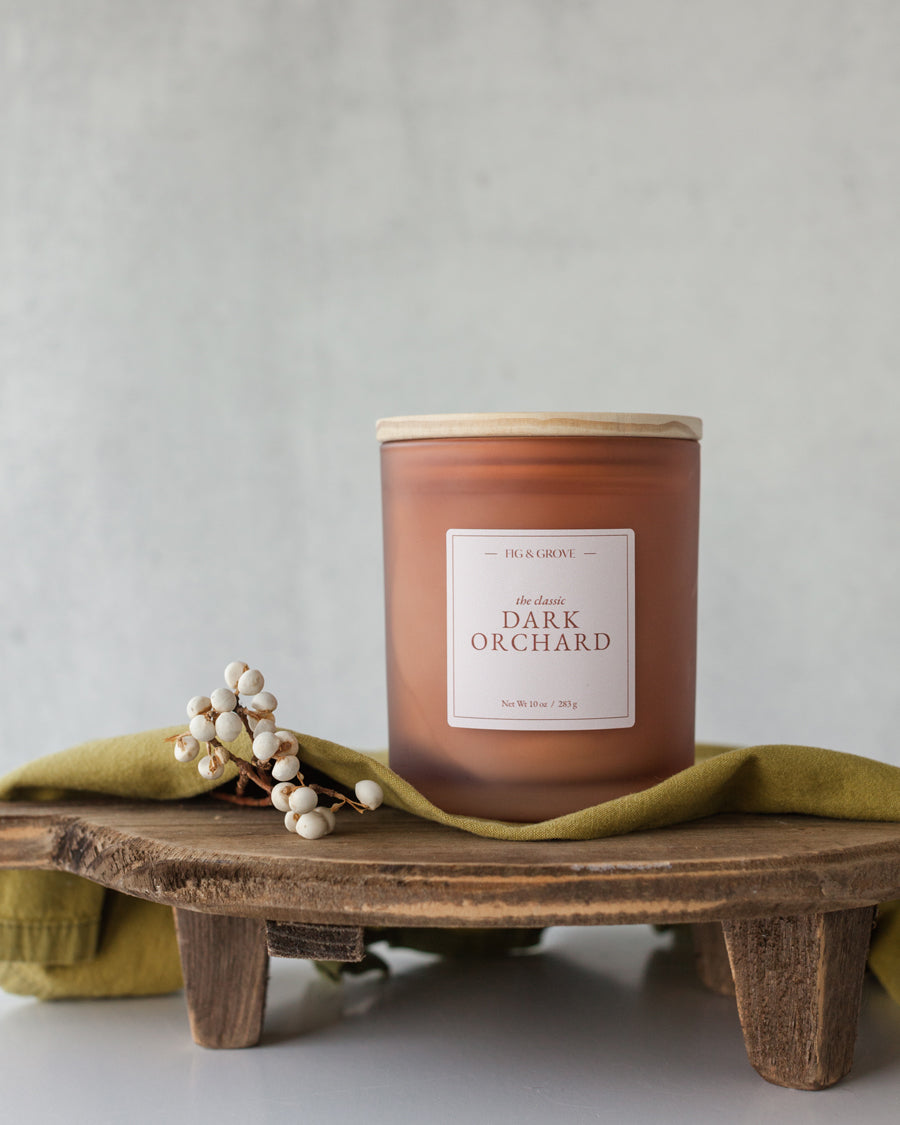 Dark Orchard candle in amber glass jar on dark wood surface, evoking cherries, spice, and candlelight – Fig & Grove
