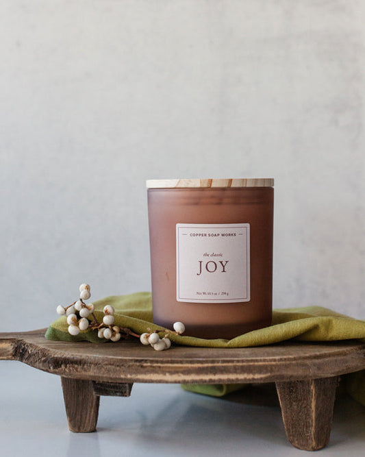 Joy candle in amber glass jar on dark wood surface, evoking floral and citrus notes – Fig & Grove
