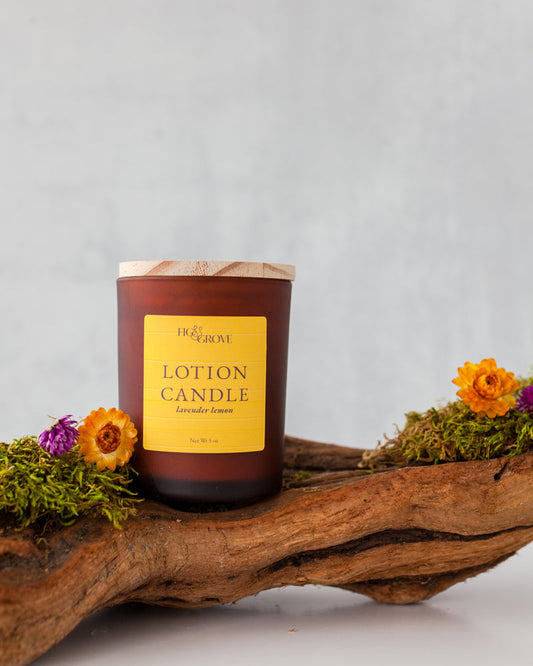 Lotion candle with a yellow label on a wooden surface with flowers and moss.