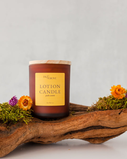 Lotion candle with wooden lid on a natural wood log with flowers against a light gray background