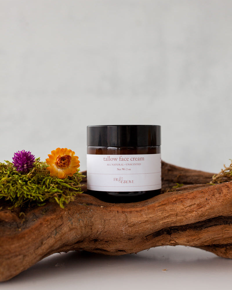 Jar of unscented regenerative suet tallow face cream for sensitive skin by Fig & Grove on a wooden log with flowers against a light background