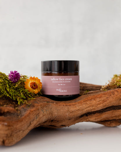 Jar of regenerative suet tallow face cream infused with yarrow & calendula by Fig & Grove on a wooden log with flowers and moss